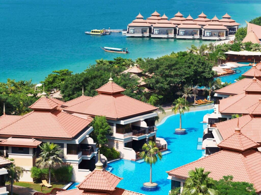 Het Anantara The Palm Dubai Resort is een tropisch toevluchtsoord met villa’s met terracotta daken, gelegen te midden van turquoise zwembaden, wuivende palmbomen en weelderig groen, aan de oever van een blauwe zee bezaaid met bungalows boven het water en boten.